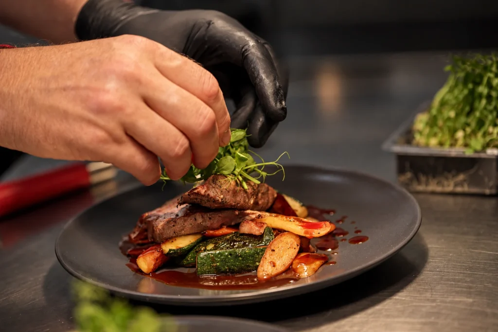 Food styling: kuchař dokončuje masový pokrm čerstvými výhonky