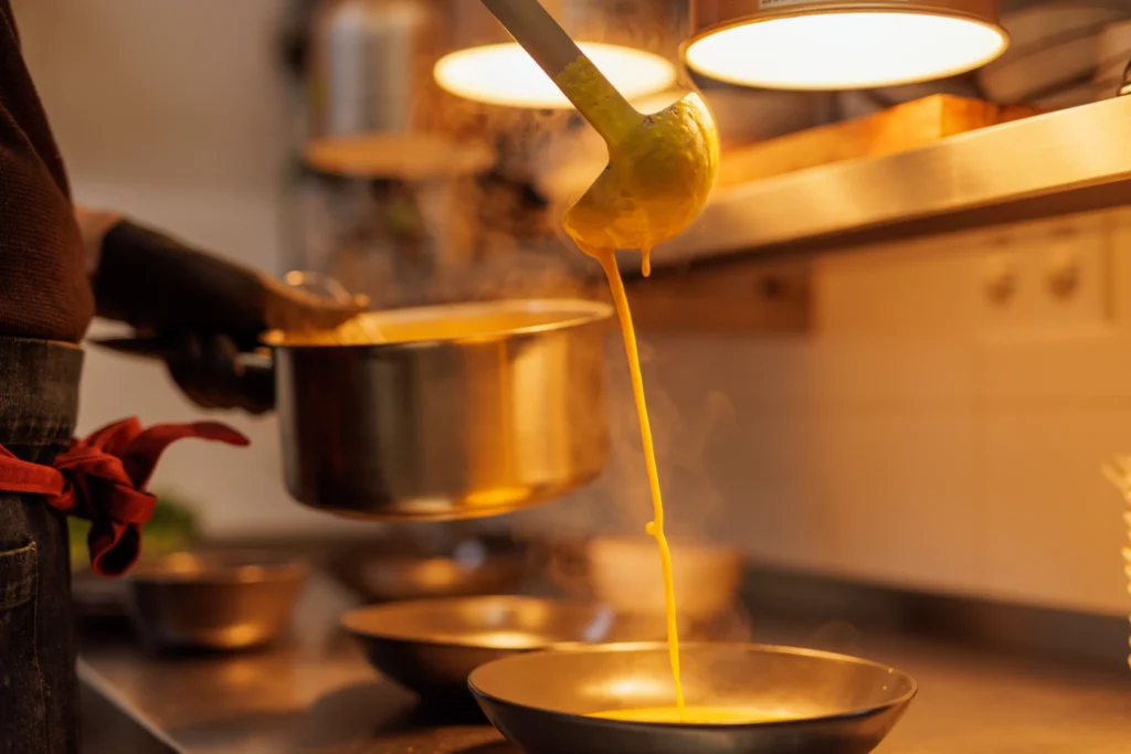 Nalévání horké polévky z naběračky v kuchyni restaurace